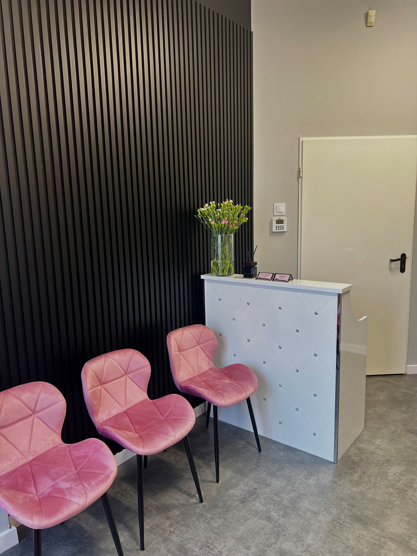 Recepcja z czarną lamelową ścianą i różowymi krzesłami